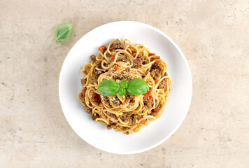 Spaghetti bolognese with fresh basil, tomatoes, garlic and parmesan cheese in a white plate on a beige background. Top view.