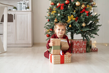 Fototapeta na wymiar cute little child girl in red pajama with gift boxes sitting under christmas tree at home