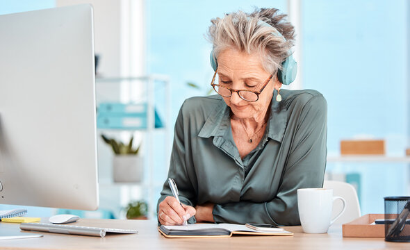 Senior Woman, Writing And Schedule In Office With Music Headphones At Desk, Reading Or Focus. Elderly Secretary, Receptionist Or Communication Executive At Table With Notebook, Pc Or Listen To Radio