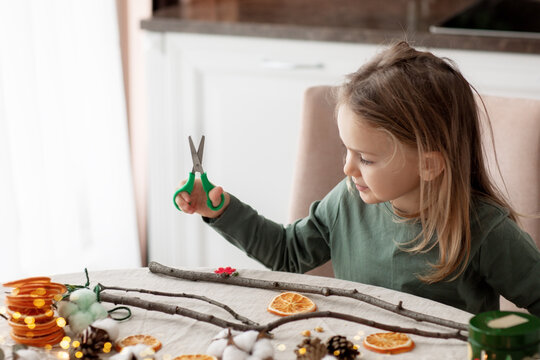 Winter holiday season. child little toddler girl making handmade Christmas garland home decorations from natural ECO materials