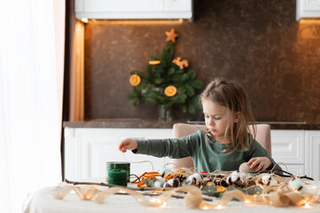 Winter holiday season. child little toddler girl making handmade Christmas garland home decorations from natural ECO materials