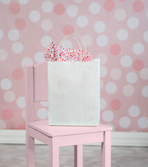 White paper party gift bag present on pink chair polka dot wall in background - 550771667