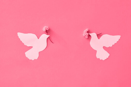 Two white pigeons, cut out of paper with live white flowers in their beaks. The concept of the International Day of Peace, do it yourself. Tinted image, color of the year 2023 viva magenta