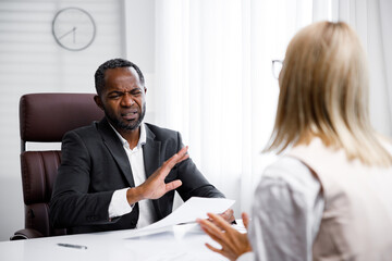 Hiring, interview. Middle aged business african american boss holding a job interview in a bright office. He looks at the resume, he does not like the employee. Refuses to apply for a job.