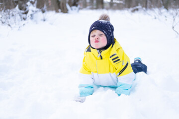 Fototapeta na wymiar Cute smiling little boy lying in a snowdrift, having fun, laughing outdoors in winter forest