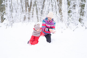 Fototapeta na wymiar Mother and daughter on winter walk in nature. woman and child girl make snowman