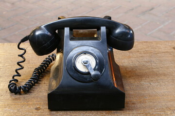 Old black antique rotary telephone on a wooden table