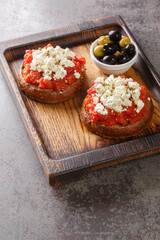 Dakos Cretan Meze appetizer with barley rusk, tomatoes, feta cheese, oregano and olive oil closeup on the wooden board on the table. Vertical