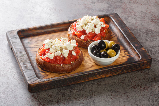 Greek dakos appetizer with barley rusk, tomatoes, feta cheese, oregano and olive oil closeup on the wooden board on the table. Horizontal