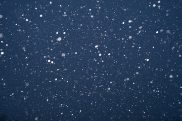Beautiful dark blue night background with falling snow. Texture of winter christmas holiday. Falling real snowflakes. Background with copy space for Christmas greeting cards or flyers design