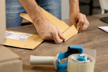 Post office worker sealing adhesive paper bag at counter indoors, closeup