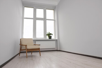 Empty renovated room with potted houseplant, armchair and windows