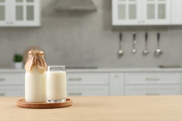 Bottle and glass with milk on wooden table in kitchen, space for text