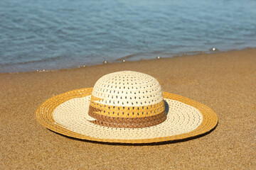 Fototapeta na wymiar Beautiful straw hat on sand near sea. Beach accessory
