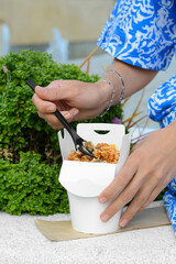 Woman eating takeaway noodles from paper box with fork outdoors, closeup. Street food