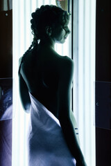 Silhouette rear view slim pretty woman enjoying tan in modern vertical solarium in SPA salon. From back lady in solarium, gets pleasure and enjoy. Concept of healthy lifestyle. Copy text space