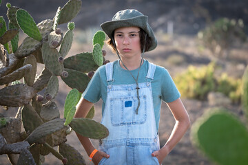 Portrait of a teenager in casual denim overalls and a hat on the background of wild cacti.
