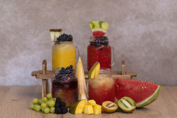 cold fruit juices or ice cream in glass jugs. four types of juices of different colours and flavours with straw surrounded by fruits such as watermelon, raspberry, kiwi, melon, with space for text.