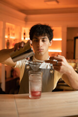 The bartender preparing a cocktail pours from a shaker into a glass using a sieve.