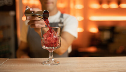 Bartender pouring alcohol into glass with ice from jigger on bar counter