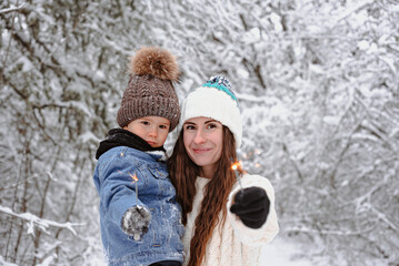 Fototapeta na wymiar Mom and son are walking in the snow and light sparklers in the forest.