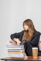 A student sits at a table with books and a glass of coffee. Beautiful long-haired girl in a jacket at a table on a white background