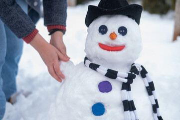 Caucasian woman sculpts a snowman from the snow. The carrot is the place of the nose.