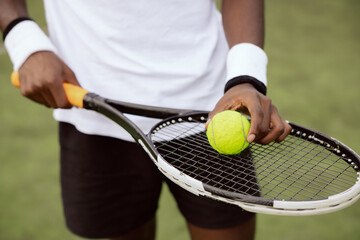 Close-up of the hands of tennis player of African appearance holding racket and placing yellow...