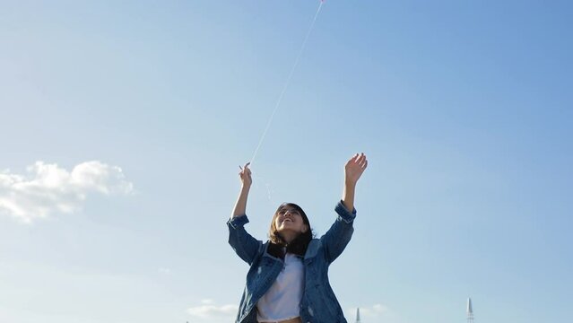 Attractive woman trys to fly lgbt kite on the beach in summer cold day. Woman wears denim jacket