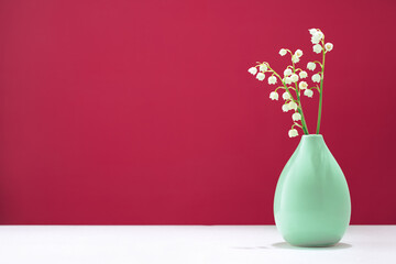 lily of the valley spring flowers in a tiny green vase on table. Vivid magenta background with copy...