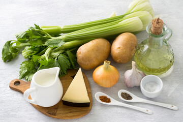 Ingredients for a vegetarian dish: stalk celery, potatoes, onions, garlic, cheese, cream, olive oil, salt, spices on a light gray background. Cooking delicious homemade food