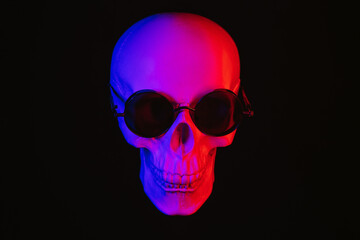 human skull wearing sunglasses with colored neon light on a dark background