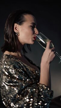 Vertical video. Beautiful brunette woman in shiny golden gress drinking champagne, and eating cake. Glamour woman celebrating New Year. Brunette sparkling lady.