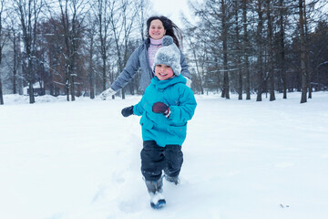 Fototapeta na wymiar Laughing boy with his mother run in the snow. Family on a walk in winter.