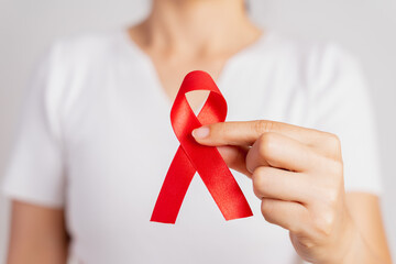 Closeup woman hand holding red ribbon HIV, world AIDS day awareness ribbon. Healthcare and medicine concept.