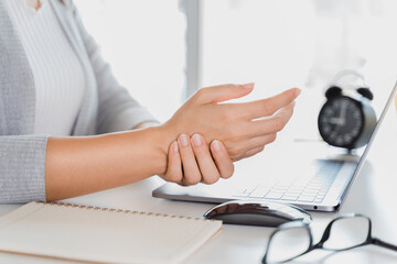 Closeup woman holding her hand pain from using laptop computer long time. Office syndrome concept.