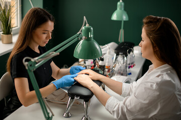 Woman manicurist looking at hands and nails of client in beauty salon.
