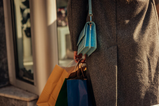 A close up photo of a girl in gray coat wearing handbag and shopping bags in her hand