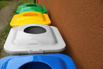 Fototapeta na wymiar Many color recycling bins near brown wall outdoors, closeup