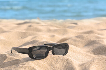 Fototapeta na wymiar Stylish sunglasses on sandy beach near sea. Space for text