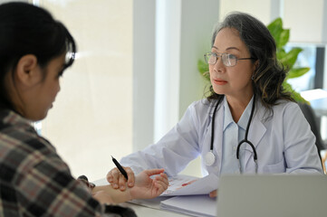 Professional Asian senior female doctor examining a patient in her cliic office, checking pulse