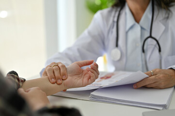 close-up, Professional Asian aged female doctor checking patient's pulse on her hand.