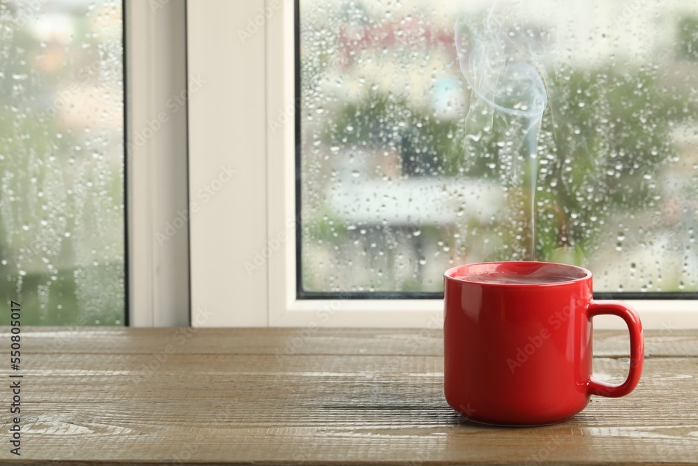 Wall mural Cup of hot drink near window on rainy day. Space for text