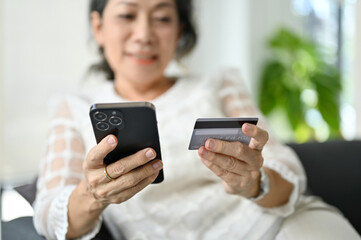 close-up, An attractive Asian retire woman using her smartphone and holding a credit card
