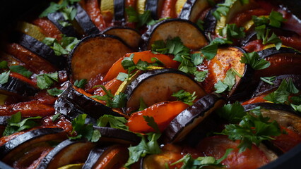 Layered ratatouille in a baking dish, slices of zucchini, red bell pepper, chili, yellow squash,...