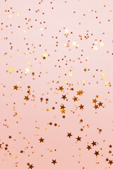 Gold colored stars and crystals confetti on a pink glittering background. Festive composition. Selective focus.