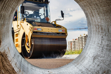 Vibratory road roller lays asphalt on a new road under construction. Close-up of the work of road construction equipment. Modern work on the construction of city streets. View from the big pipe.