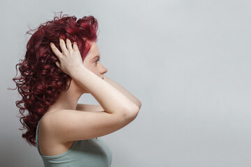 Obraz premium Beautiful woman touching her red curly hair against white background