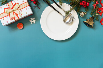 Flat lay of Christmas table setting with plate, cutlery, gifts boxs and christmas decorations on green background. Copy space.