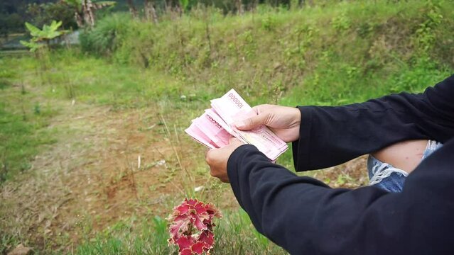 A man is counting one hundred thousand rupiah bills outside the room
